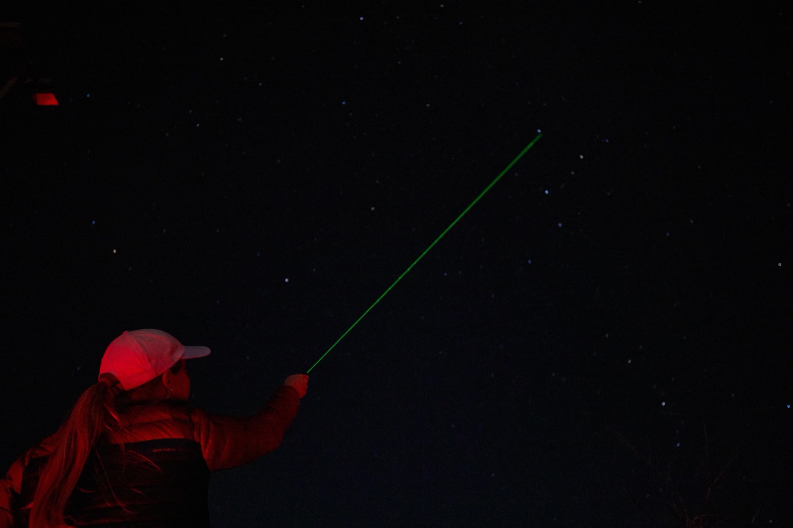 A tour guide working under red light points a green laser at constellations above Bryce Canyon