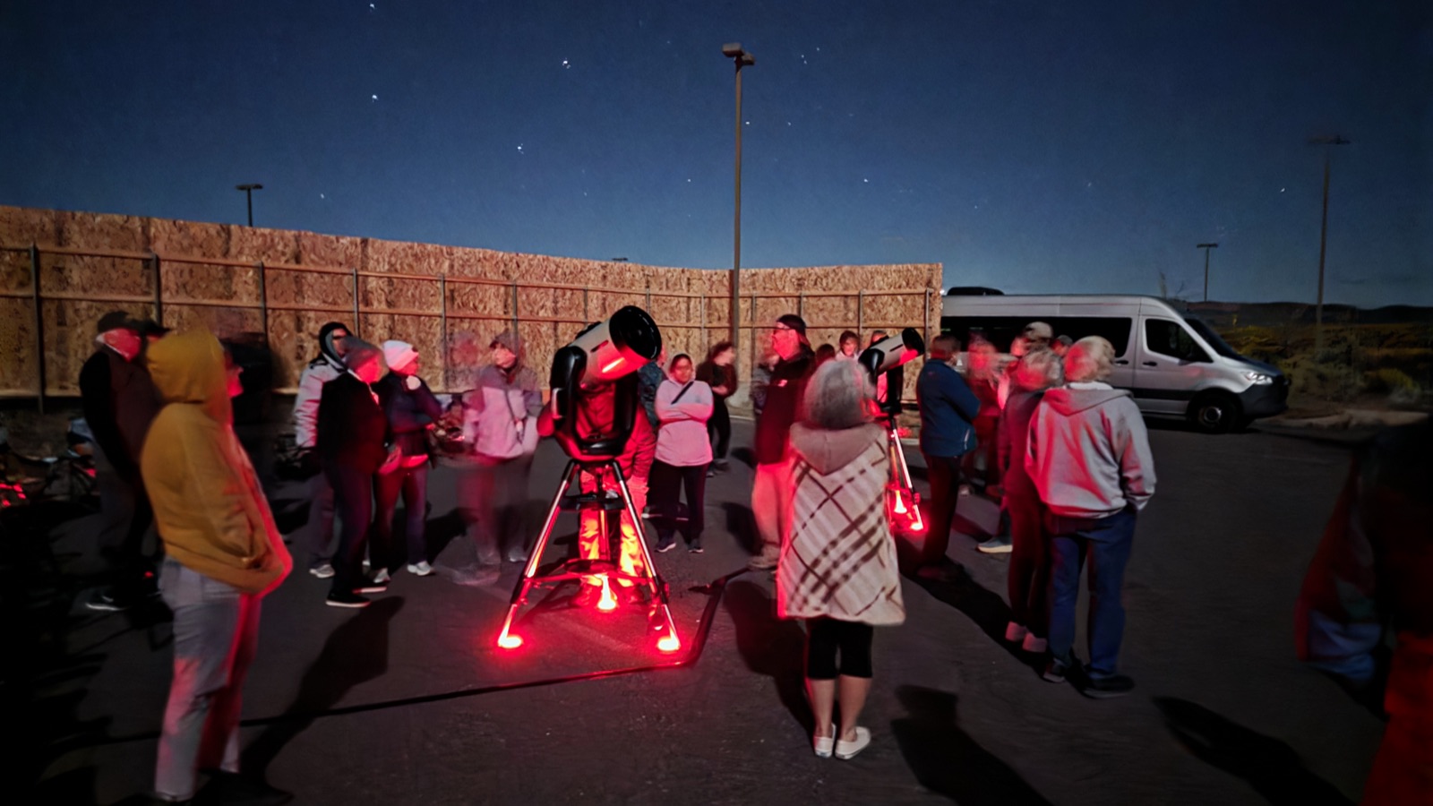A guided tour group gathered around a telescope at dusk beside the tour van near Bryce Canyon